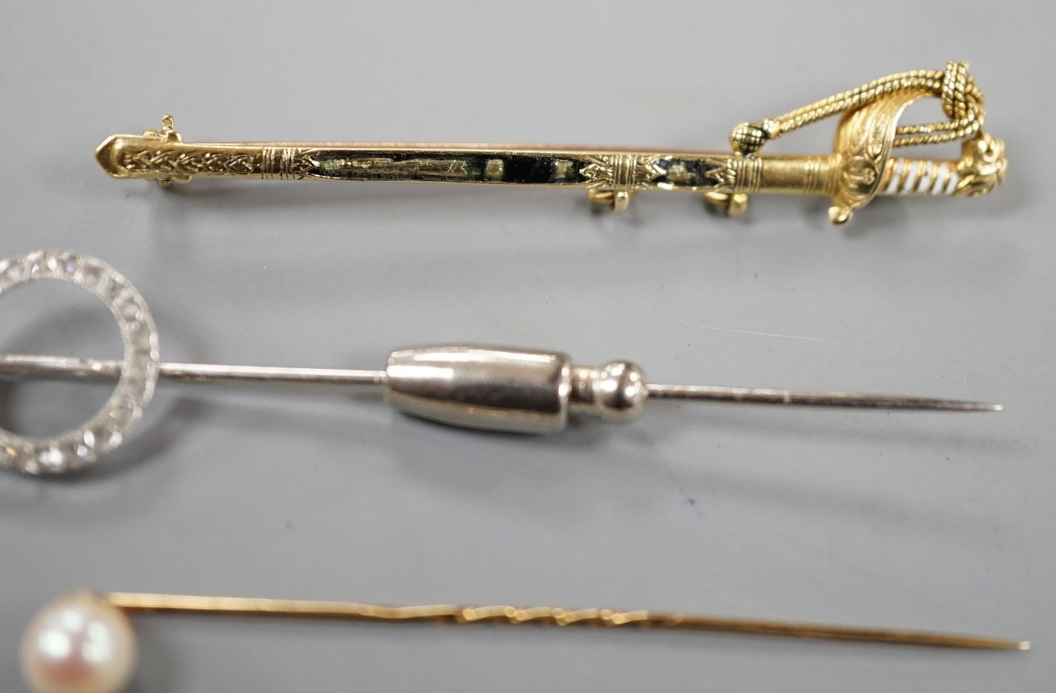 A French white metal (poincon mark for platinum) and diamond set tie pin, 64mm, gross 3.4 grams, a 15ct and enamel(a.f.) sword brooch, gross 4.7 grams and toe 9ct pins, one with cultured pearl, gross 3 grams.